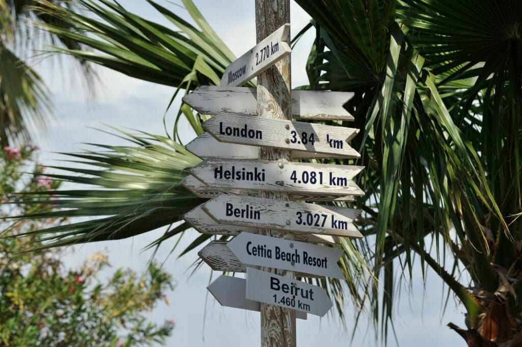 A rustic signpost in a tropical setting points to major global destinations, hinting at wanderlust.