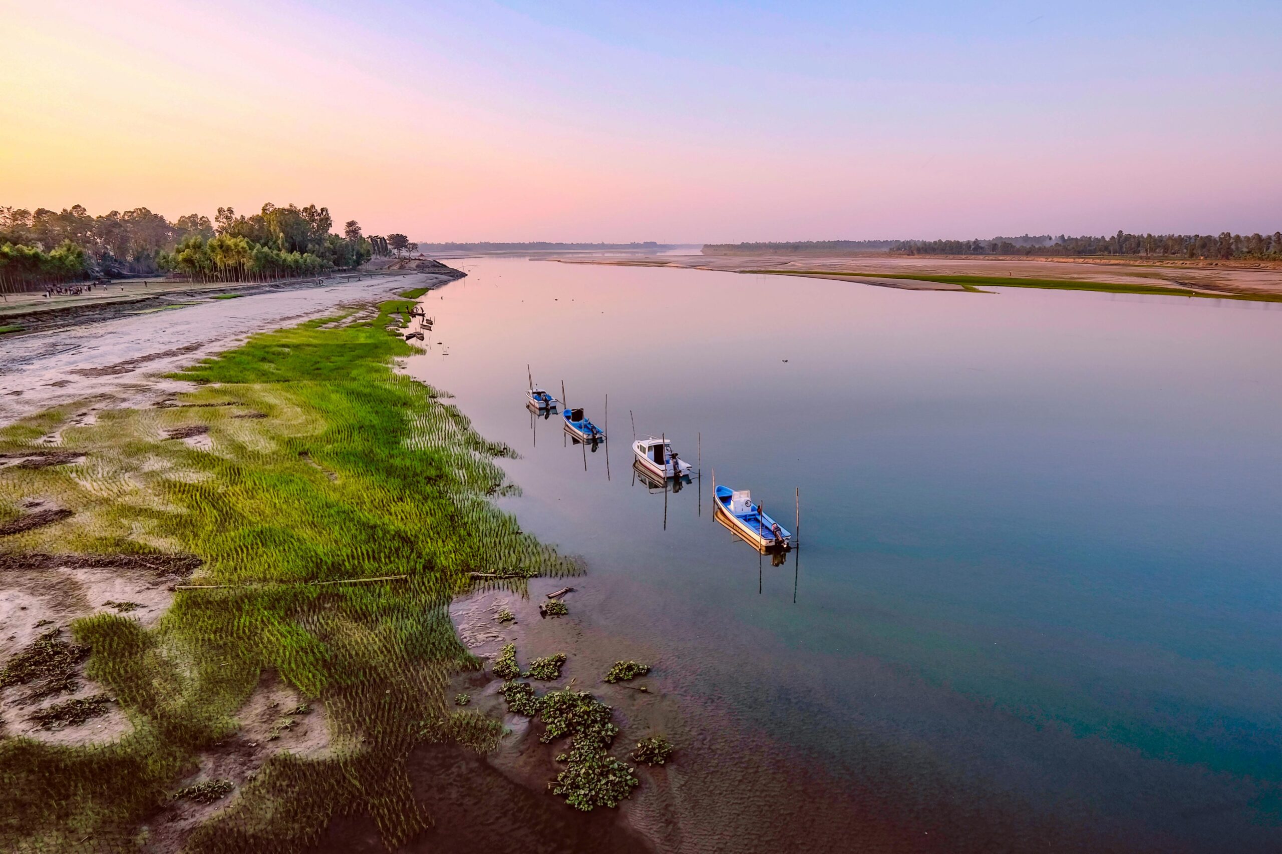 Top 12 Undiscovered River Cruises to Unveil Hidden Worlds Tranquil river view in Kurigram, Bangladesh with boats and lush greenery at dawn.