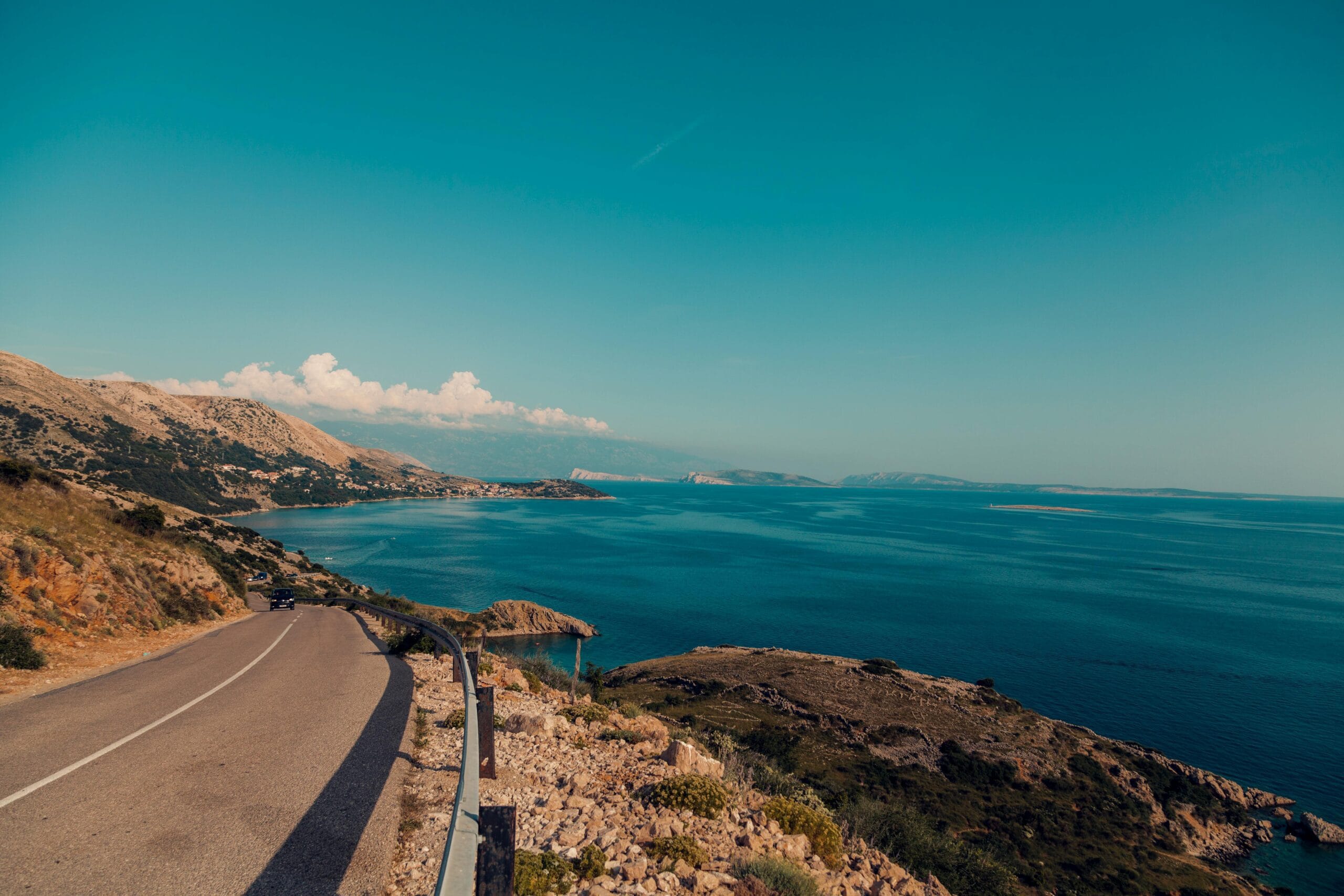 Breathtaking view of a coastal road alongside the ocean with clear blue skies and rugged terrain.