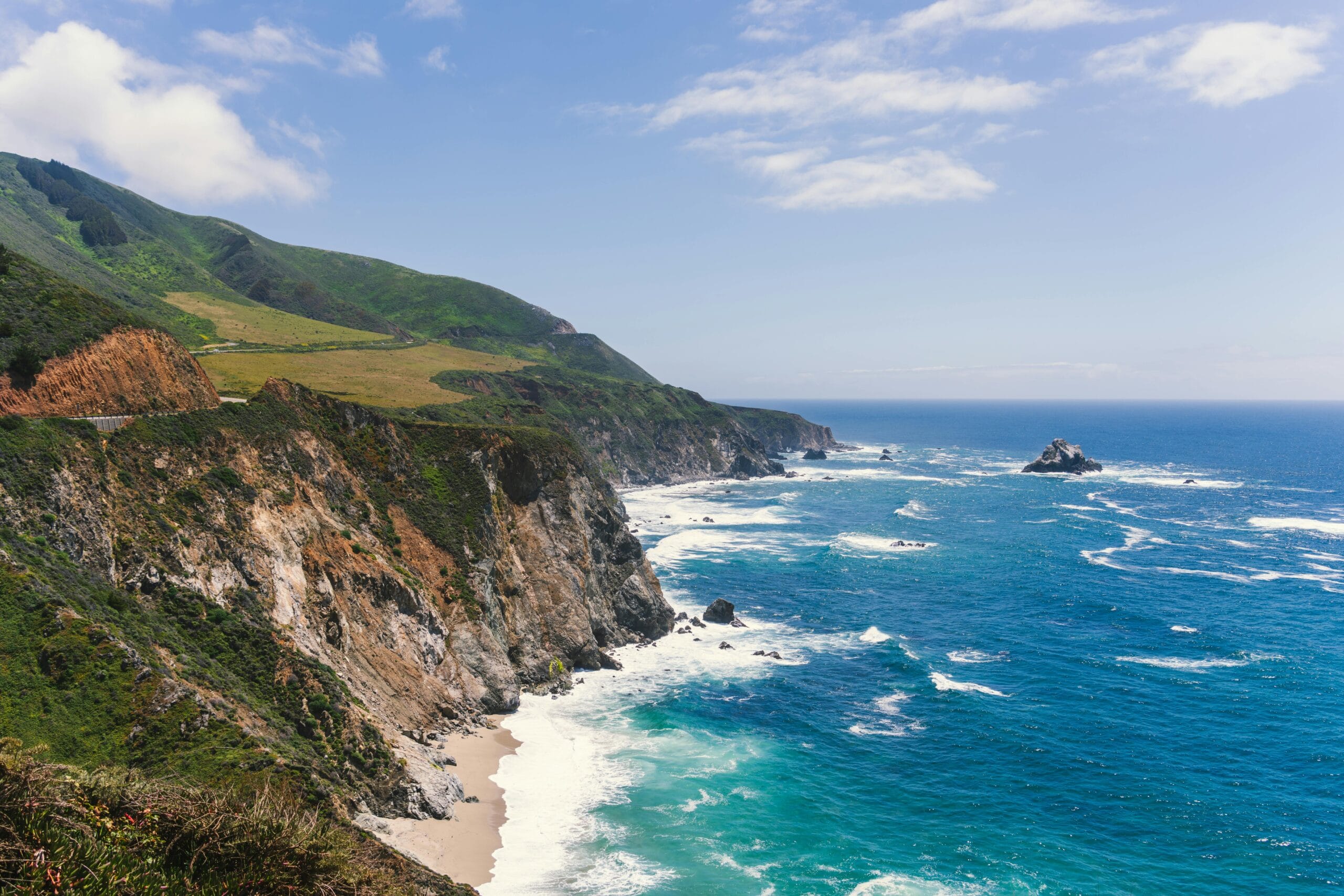 Dramatic coastal cliffs of Monterey, California against a vibrant ocean under a blue sky.