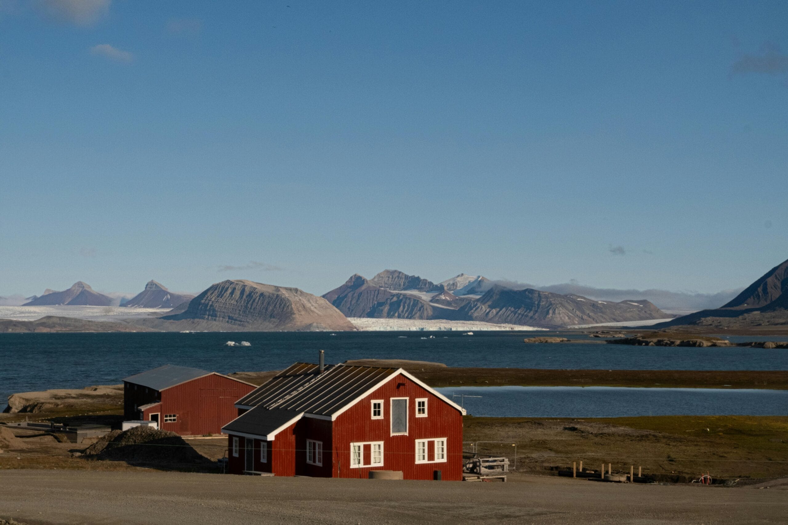 Serene view of a red cabin against a backdrop of Arctic mountains and sea.