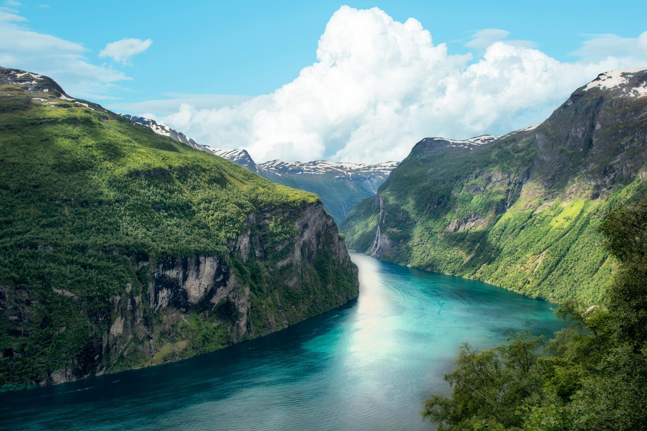 Breathtaking aerial view of a vibrant Norwegian fjord with lush cliffs and clear skies.