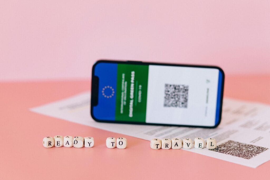 Smartphone displaying digital green pass on a pink surface with travel beads.